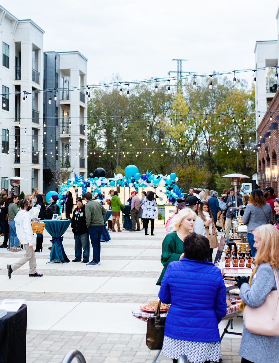 A lively outdoor market with people browsing vendors and string lights overhead in a plaza.