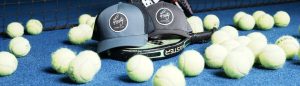 Two caps and a paddle on a blue court surrounded by tennis balls near a net.