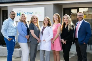 Seven smiling professionals stand together outside a building with a "New Life Health" sign.