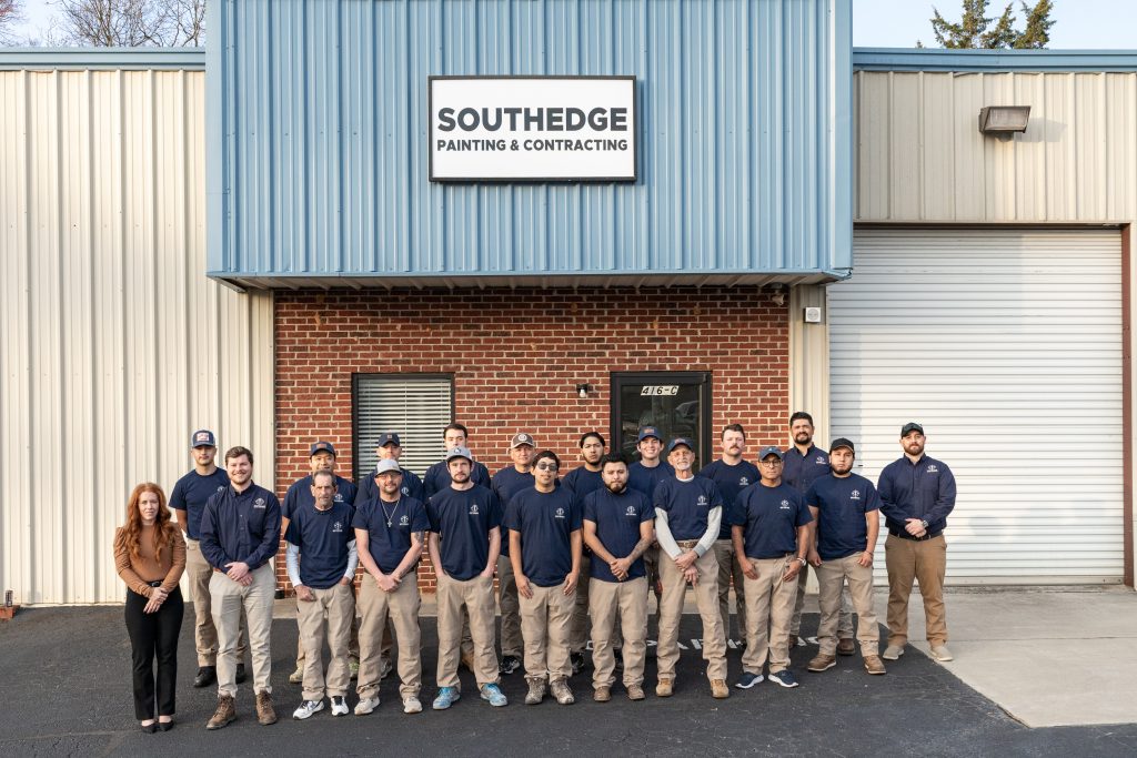 A group of sixteen people pose outside a building with a "SouthEdge Painting & Contracting" sign.