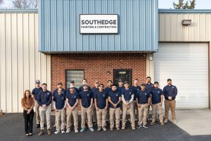 A group of sixteen people pose outside a building with a "SouthEdge Painting & Contracting" sign.
