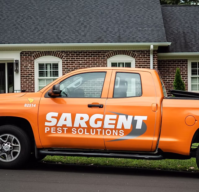 Orange Sargent Pest Solutions truck parked in front of a brick house with white trim and green lawn.