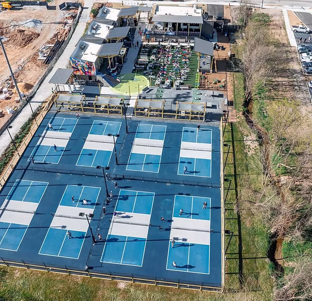 Aerial view of multiple blue pickleball courts next to a lively outdoor restaurant and seating area.