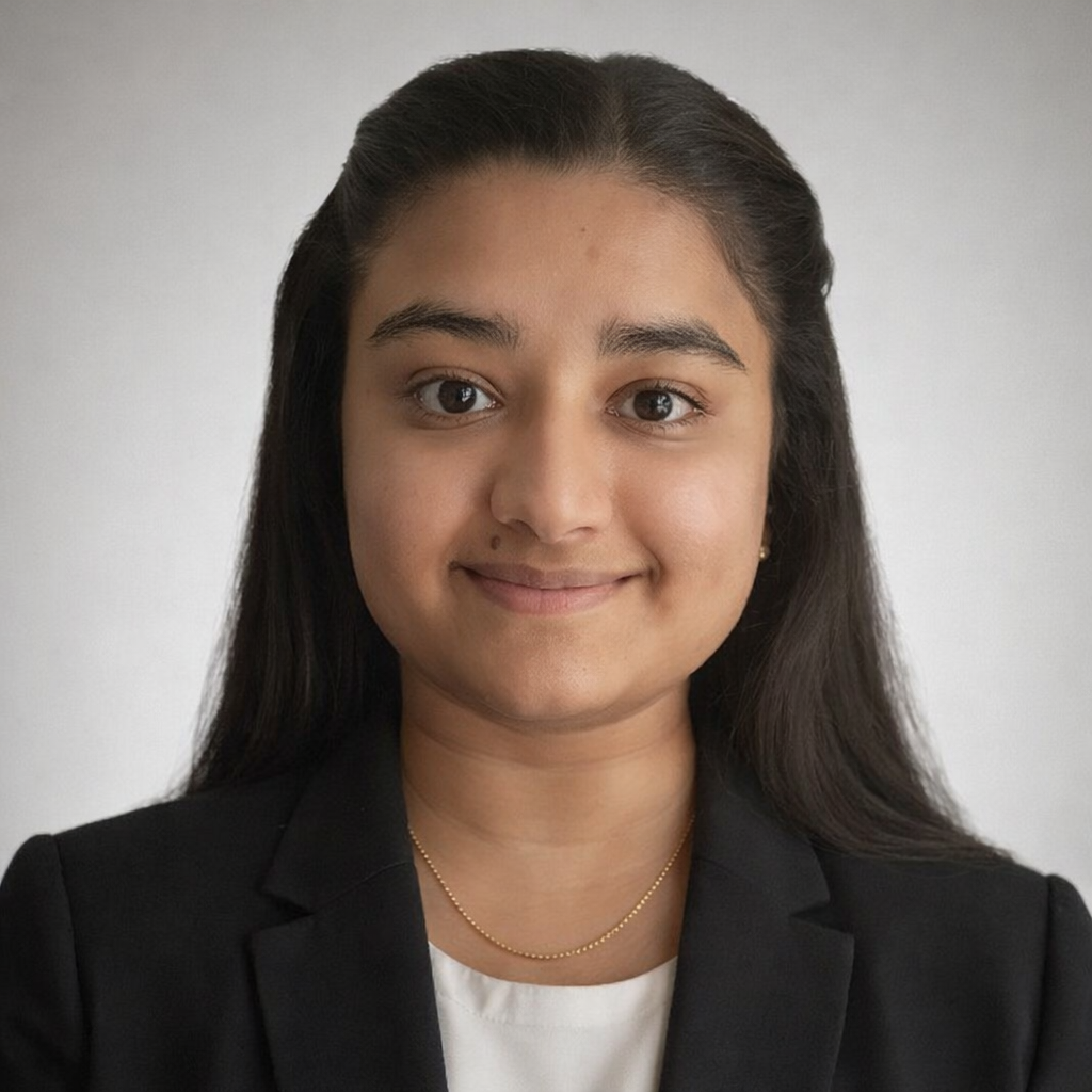 Young woman with long dark hair, wearing a black blazer and white top, smiling against a plain background.