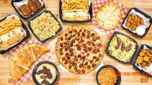 Various Italian-American dishes including pizza, salads, pasta, fries, breadsticks, and chicken, on a wooden table.