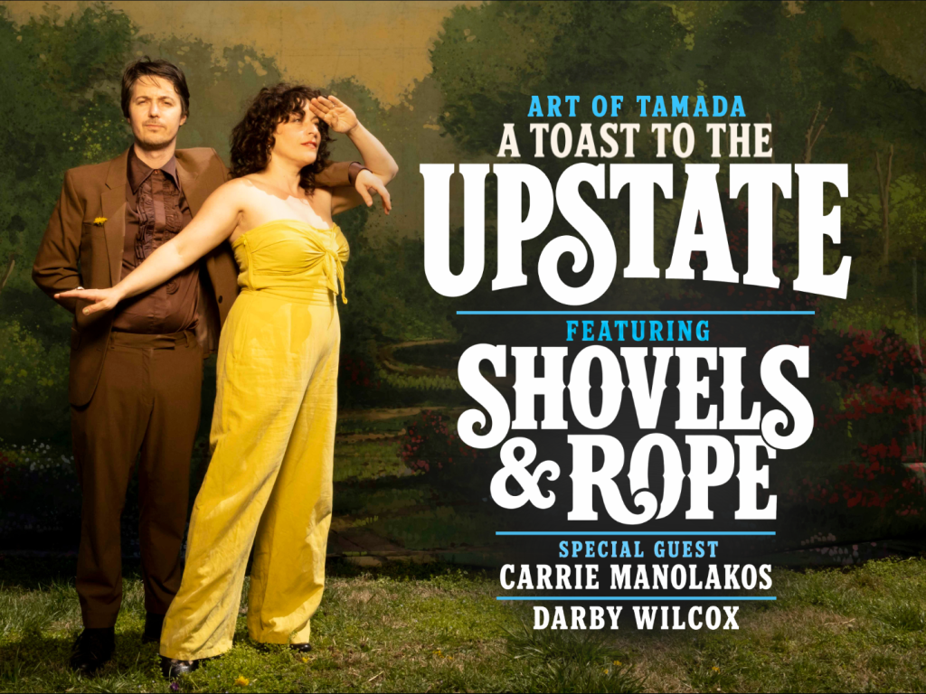 A man in a brown suit and a woman in a yellow jumpsuit pose by event text for "A Toast to the Upstate.