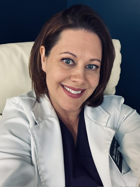 Woman in a white lab coat smiling at the camera while sitting on a white chair.