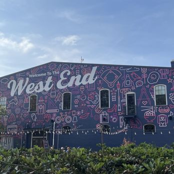 A blue building with “Welcome to the West End” painted, decorated with pink outlined icons and symbols.