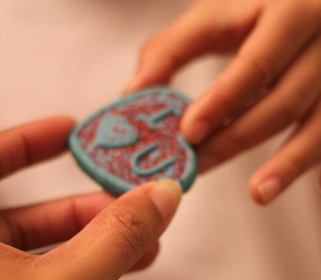 Two hands exchanging a blue and red heart-shaped cookie decorated with the word “LOVE”.