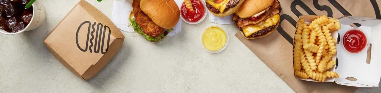 Burgers, fries, a drink, and sauces are arranged on a table with branded packaging.