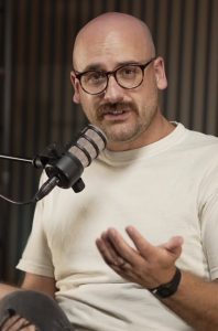 A man with glasses and a mustache speaking into a microphone.
