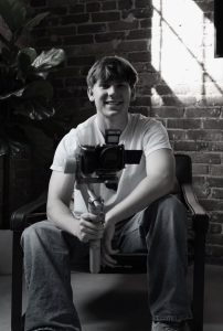 A young man sitting in a chair holding a camera mounted on a stabilizer.