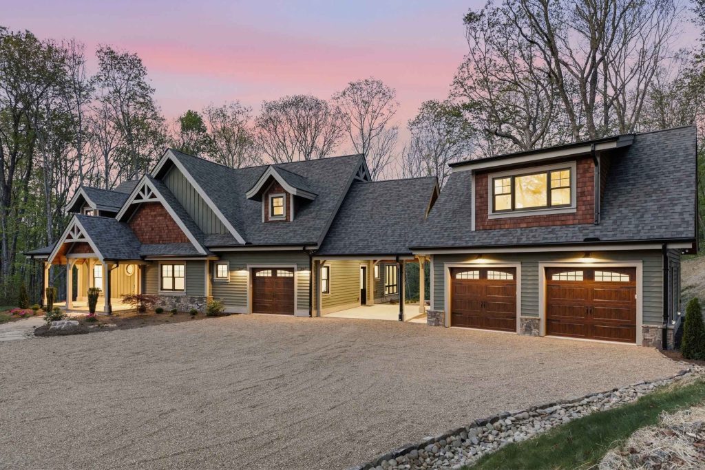 A multi-gable house with green siding, a three-car garage, and a gravel driveway at dusk.