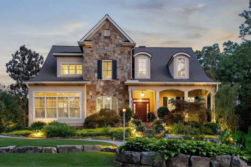 A two-story stone and siding house with a front porch, surrounded by a landscaped lawn at dusk.